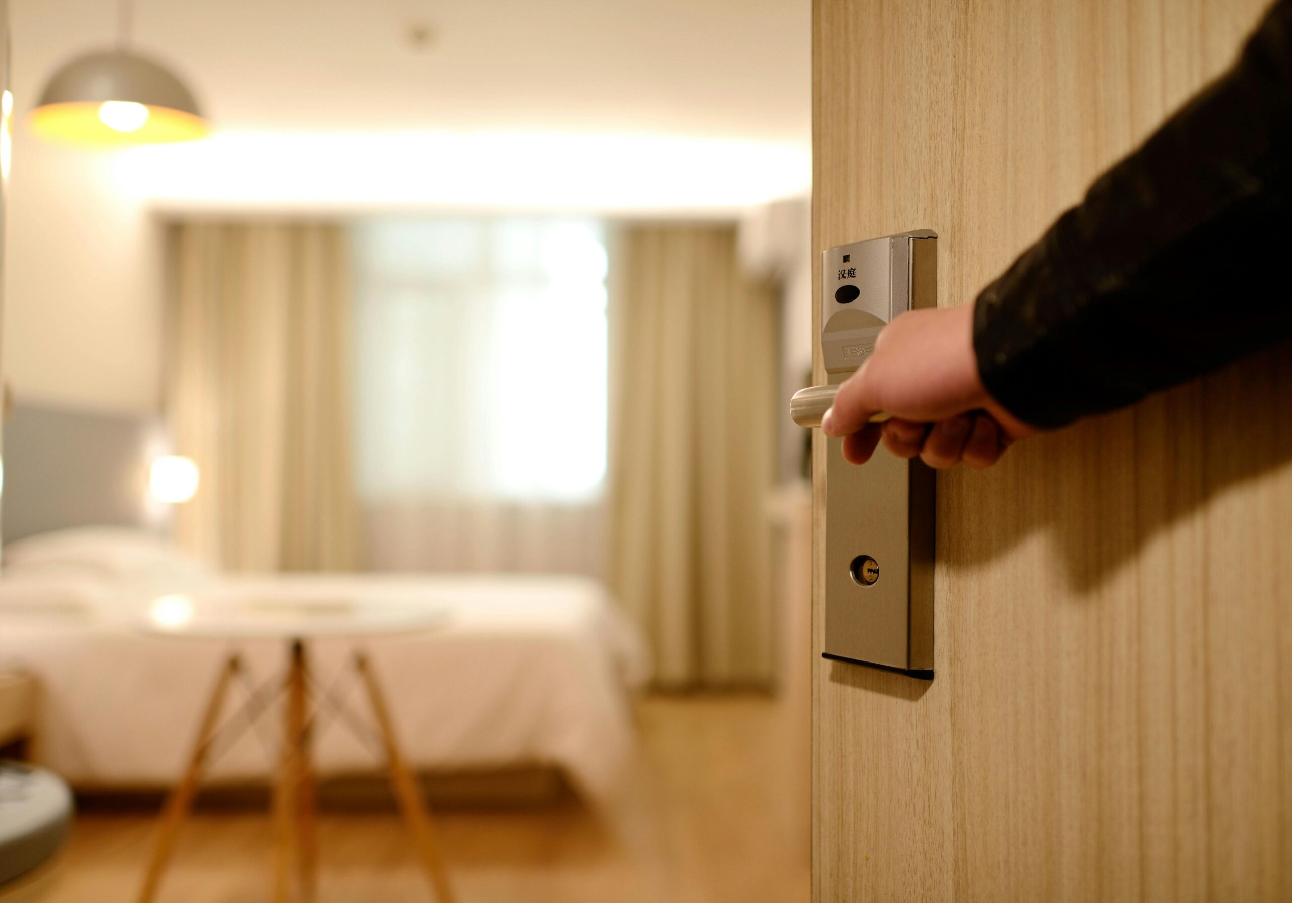 A person opens the door to a modern hotel room with a cozy bed and soft lighting, symbolizing the hospitality industry and the potential business opportunities for hotel owners with the help of hotel financing.