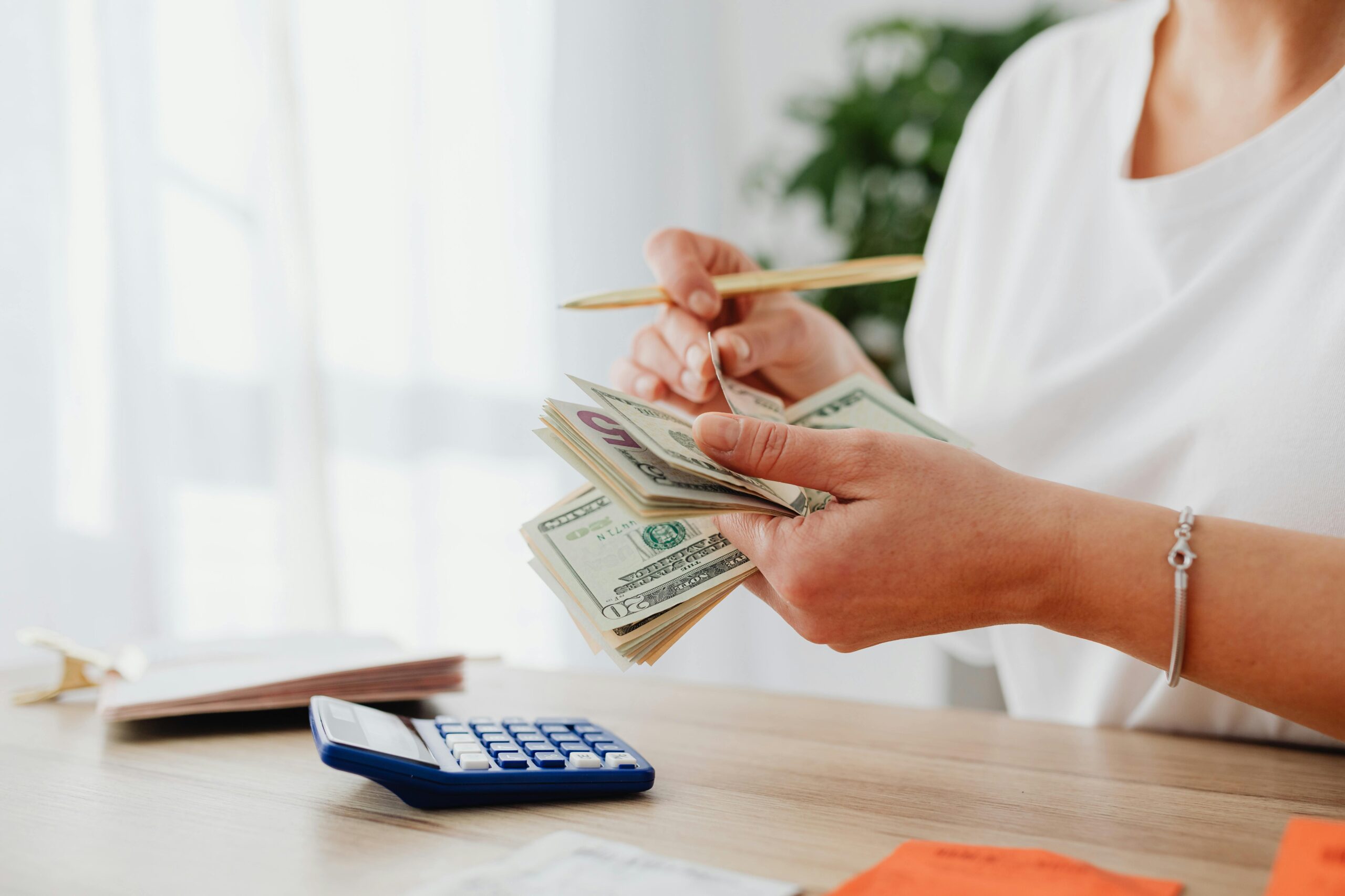 A business owner calculating expenses with a stack of cash and a calculator on the desk, demonstrating the use of unsecured working capital loans for daily business operations.