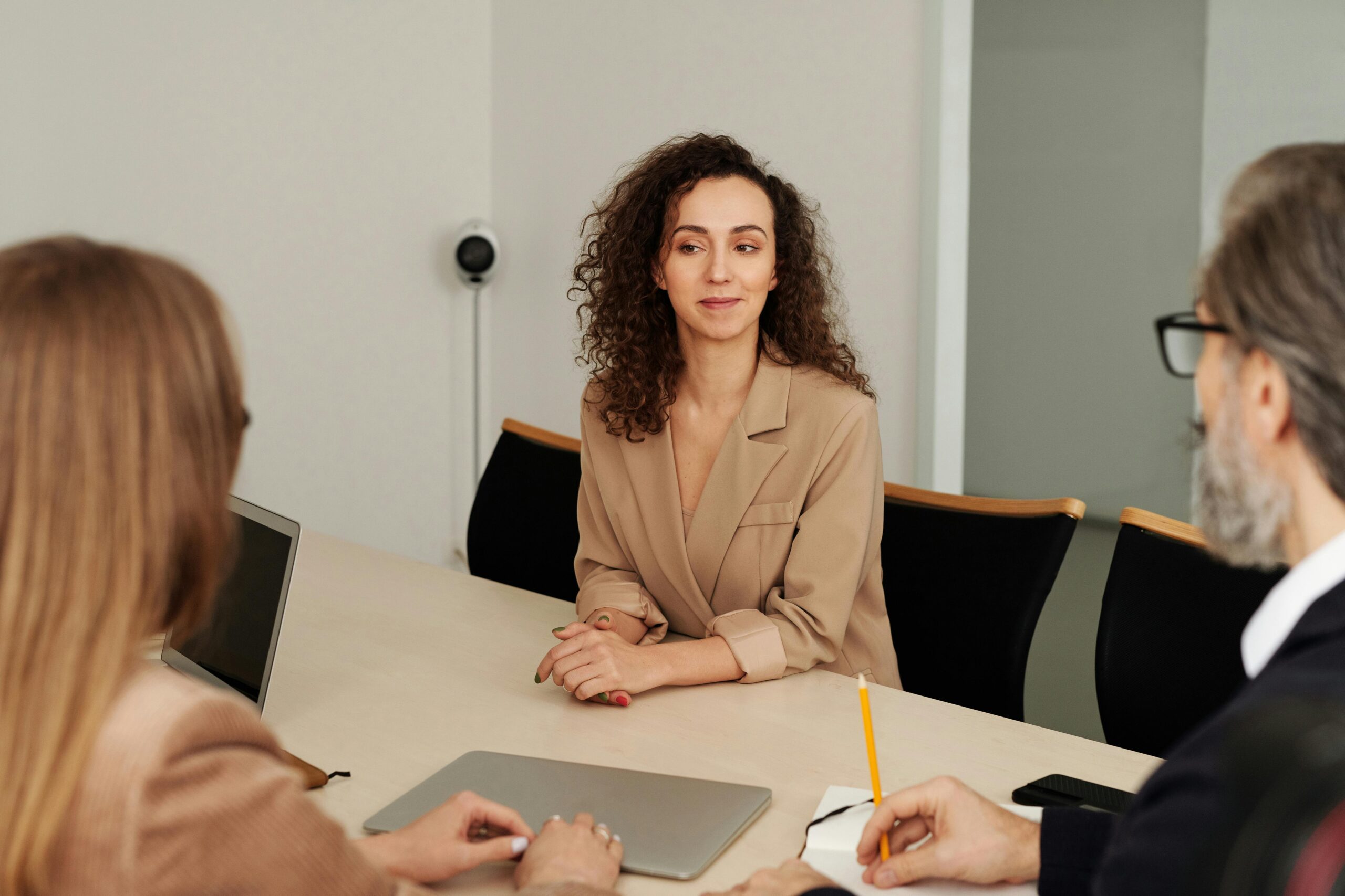 A professional businesswoman in a beige blazer sitting at a conference table during a loan application discussion, representing the process of securing commercial loans for business.